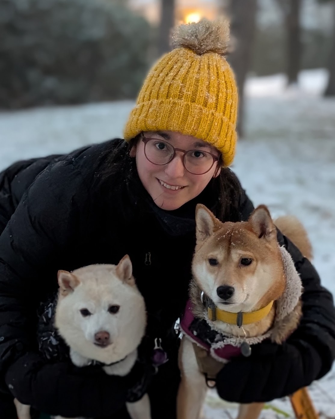 Paola in the snow with her two dogs, wearing a yellow beanie